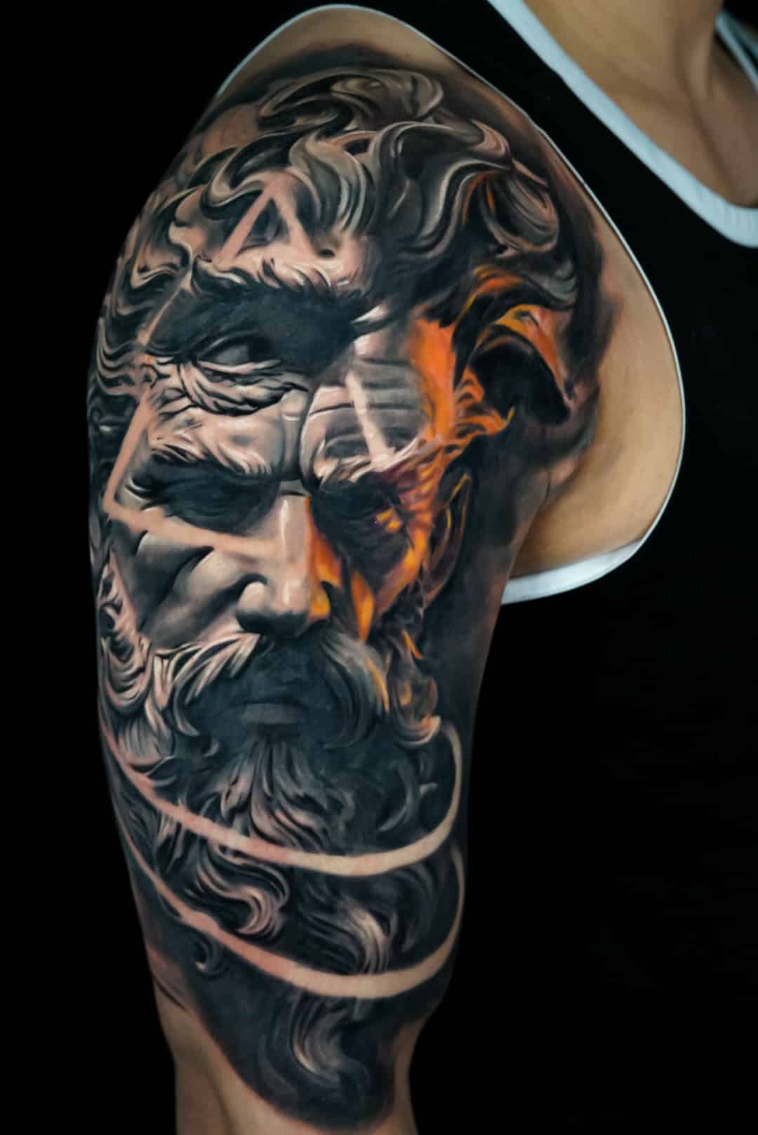 Jose Carlos 14 A detailed tattoo on an arm depicts a stone-like face with a beard, partially obscured by orange flames.
