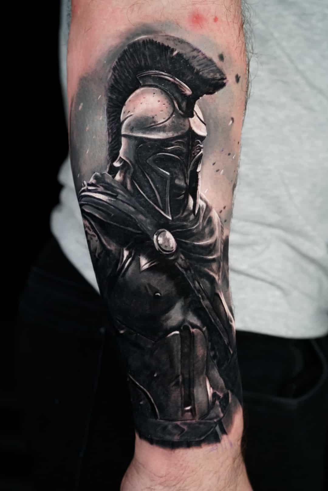 Jose Carlos 22 A grayscale tattoo of a Spartan warrior in full armor and cape, with a feathered helmet, on a man's arm.