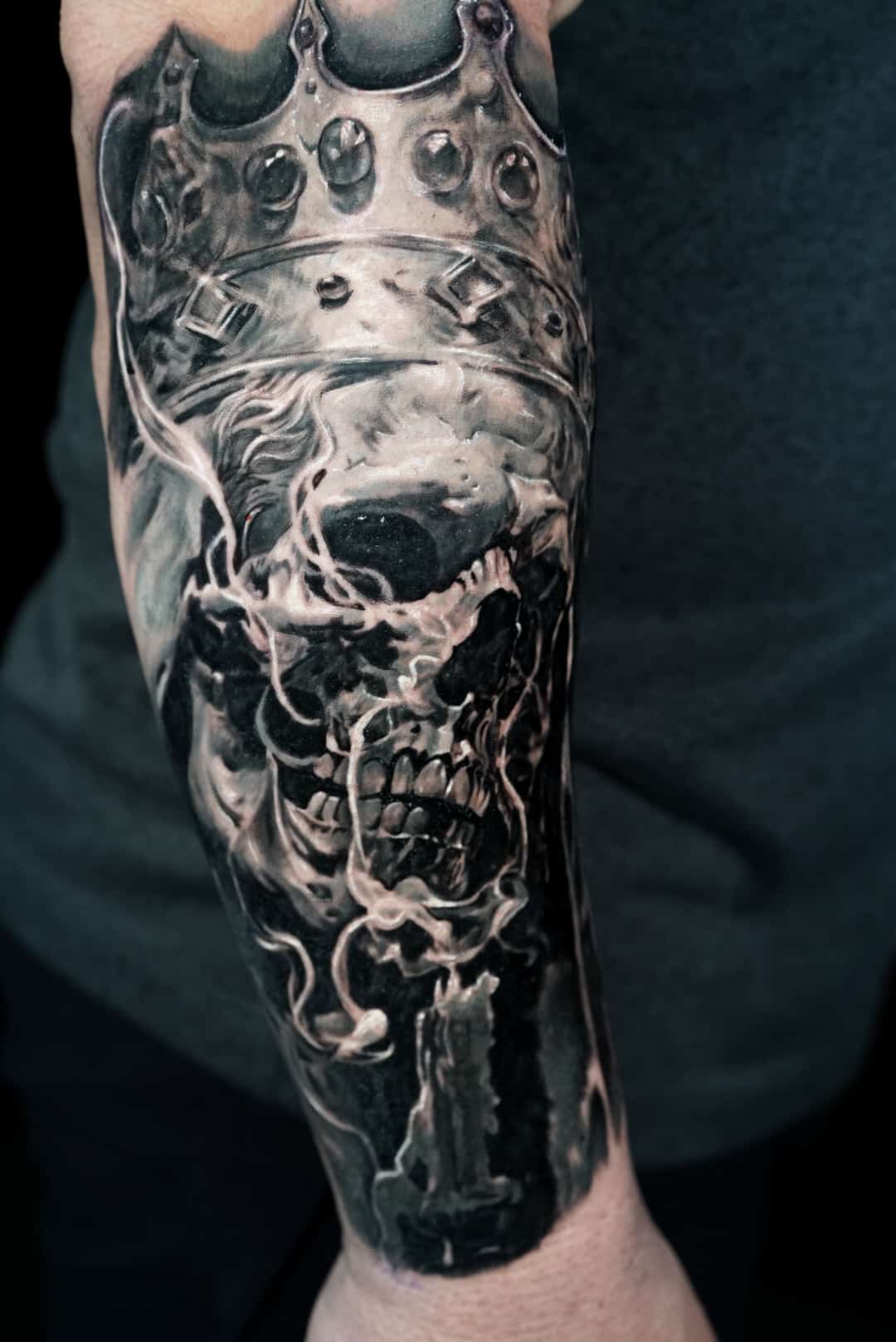 Jose Carlos 26 A black and white tattoo of a skull wearing a crown, with smoke and a candle on a person's arm.