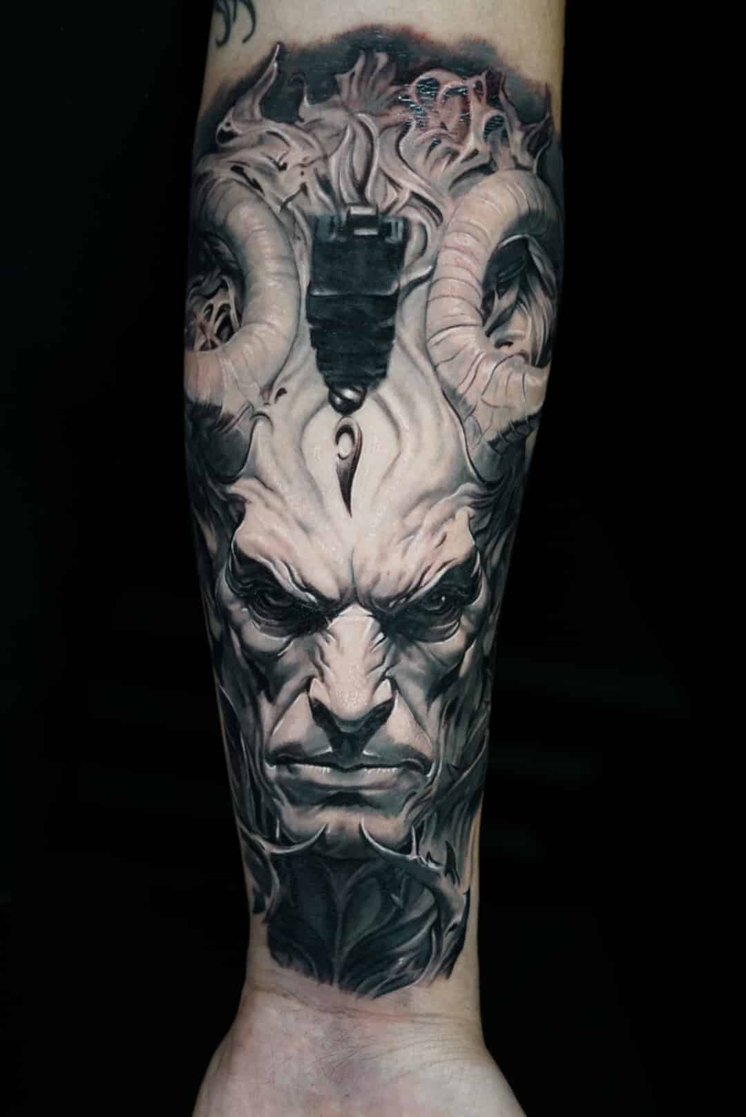 Jose Carlos 28 A detailed black and gray tattoo of a horned, demonic face with an intense, angry expression on an arm.
