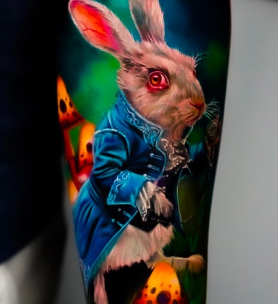 A vibrant tattoo of a white rabbit in a blue coat, with red eyes and pink ears, holding a pocket watch.