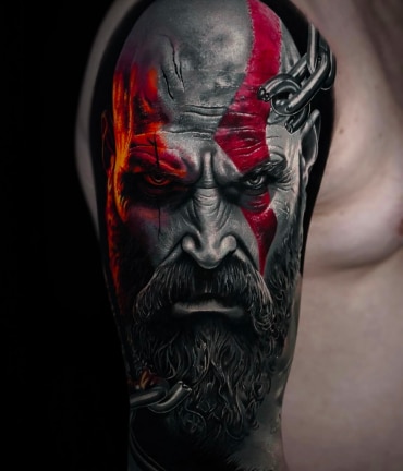 A detailed tattoo of Kratos from God of War covers an arm, featuring his red mark and chains.