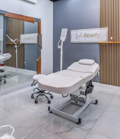 A modern beauty treatment room with a white adjustable bed, rolling stool, and a sign reading "Lala Beauty".