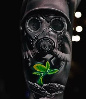 A realistic black and grey tattoo of a gas mask and helmet with a vibrant green plant growing below.