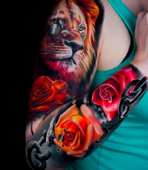 A woman's arm is covered in colorful tattoos of a lion, red and orange roses, and dark chains.