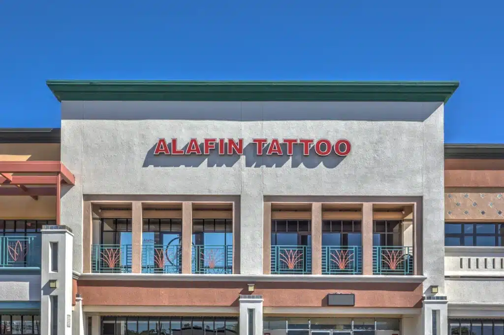 A building with a "ALAFIN TATTOO" sign in red letters above windows with decorative teal and orange railings.