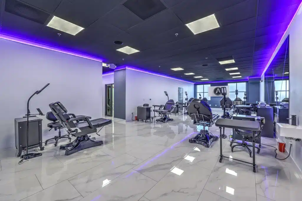 A clean, modern tattoo parlor with white walls, black ceiling, and purple LED strip lighting.