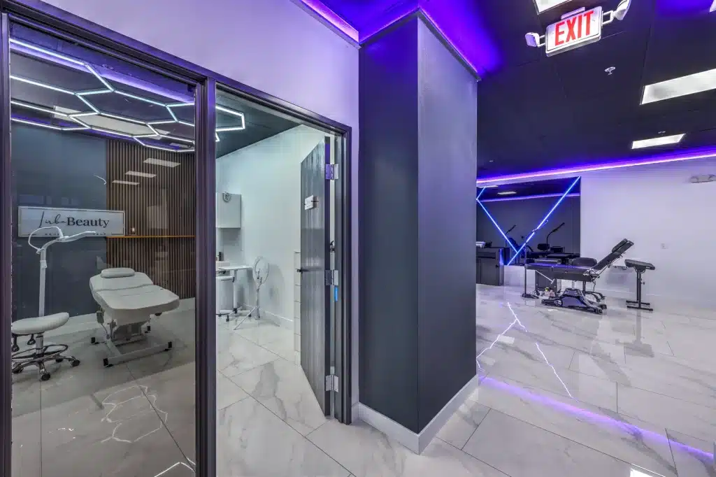 A modern beauty salon with purple accent lighting, a treatment room with "Lala Beauty" on the wall, and a black tattoo chair.