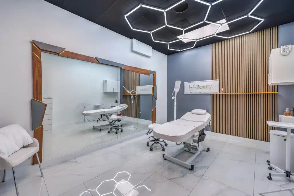 A modern beauty salon with a treatment bed, large mirror, and "Lab Beauty" sign on a gray wall.