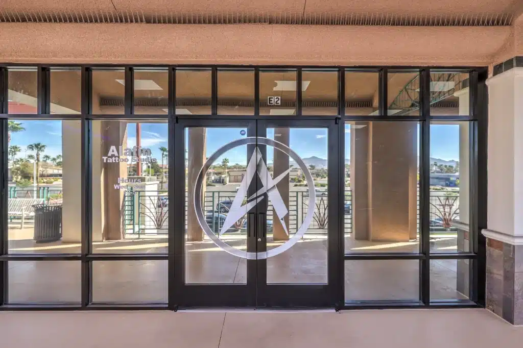 A glass storefront with "Alafin Tattoo Studio" and "Hours Wed-Sun" on the left, and a large "A" logo on the doors.