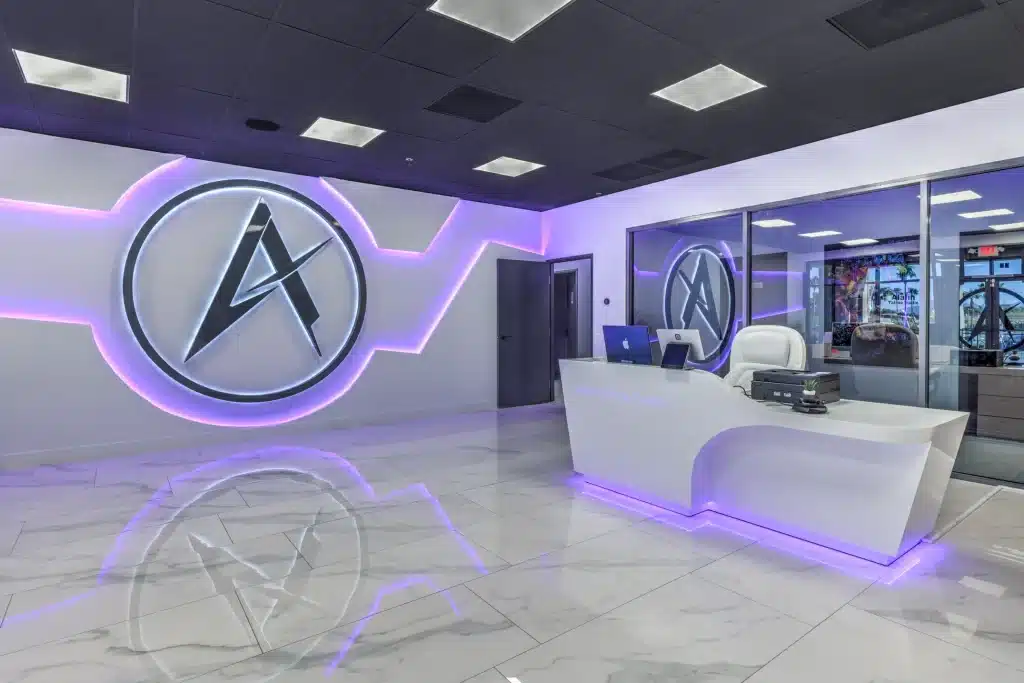 A modern reception area with a white desk, purple LED lighting, and a large "A" logo on the wall.