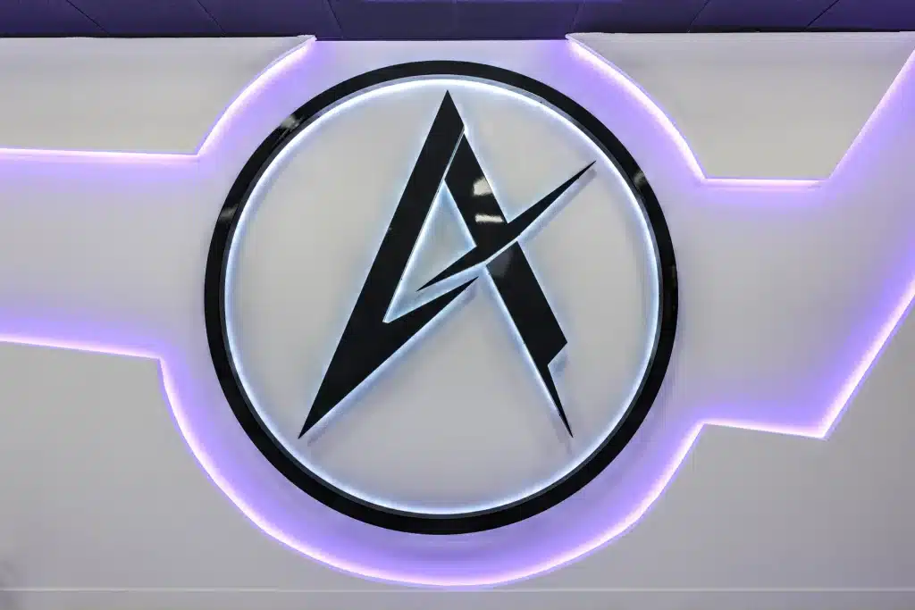 A black "A" logo with a lightning bolt through it is centered in a white circle with purple backlighting.