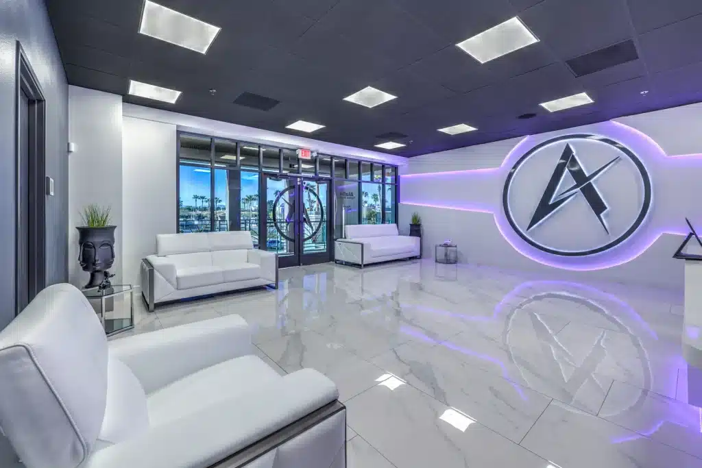 A modern lobby with white sofas, shiny white floors, and a large "A" logo on a wall with purple backlighting.