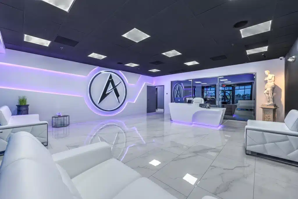 A modern reception area with white furniture, a black ceiling, and a prominent "A" logo with purple backlighting.
