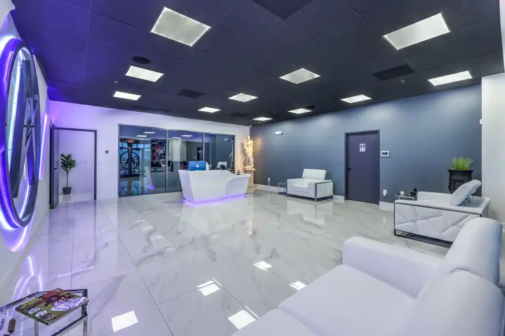 A modern reception area with white marble floors, a glowing white desk, and white seating.