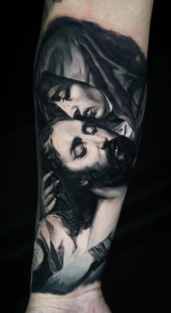 A black and white tattoo of a woman in a veil holding a man with closed eyes on her lap.