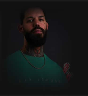 A man with a beard, neck tattoos, and a gold chain wears a teal shirt with "AIR JORDAN" faintly visible.